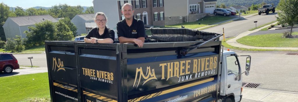 Friendly junk removal workers standing in the bed of their dump truck